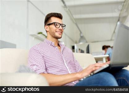 business, education, technology and people concept - smiling young man with laptop computer working at office. smiling man with laptop working at office
