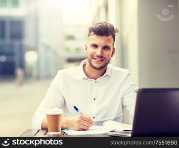 business, education, technology and people concept - young man with laptop computer, documents and coffee cup at city street cafe. man with laptop and coffee at city cafe