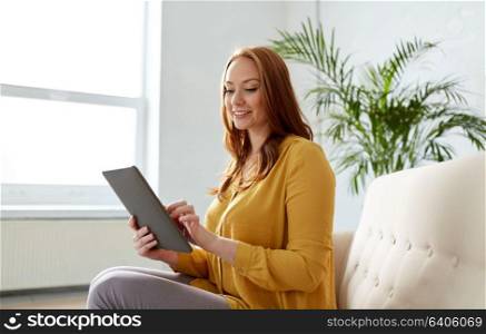 business, education, technology and people concept - young redhead woman with tablet pc computer working at office. smiling woman with tablet pc sitting on sofa