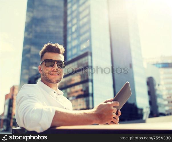 business, education, technology, communication and people concept - happy smiling man in sunglasses with tablet pc computer sitting on city street bench. man with tablet pc sitting on city street bench