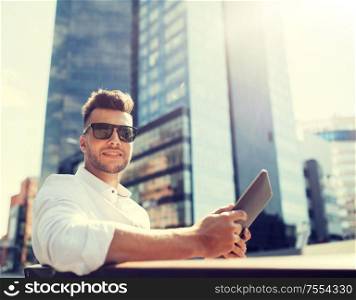 business, education, technology, communication and people concept - happy smiling man in sunglasses with tablet pc computer sitting on city street bench. man with tablet pc sitting on city street bench