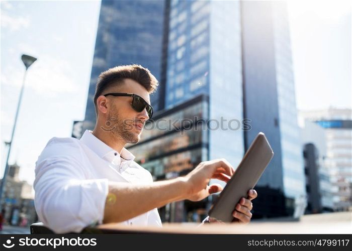 business, education, technology, communication and people concept - man in sunglasses with tablet pc computer sitting on city street bench