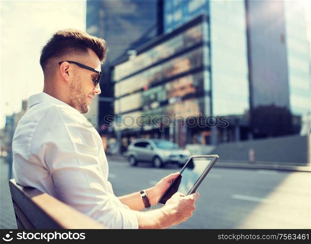 business, education, technology, communication and people concept - man in sunglasses with tablet pc computer sitting on city street bench. man with tablet pc sitting on city street bench