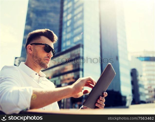 business, education, technology, communication and people concept - man in sunglasses with tablet pc computer sitting on city street bench. man with tablet pc sitting on city street bench
