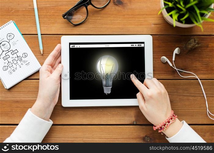 business, education, technology, people and inspiration concept - close up of woman with light bulb icon on tablet pc computer screen on wooden table
