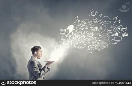 Business education. Young businessman with opened book in hands blowing on pages