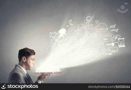 Business education. Young businessman with opened book in hands blowing on pages