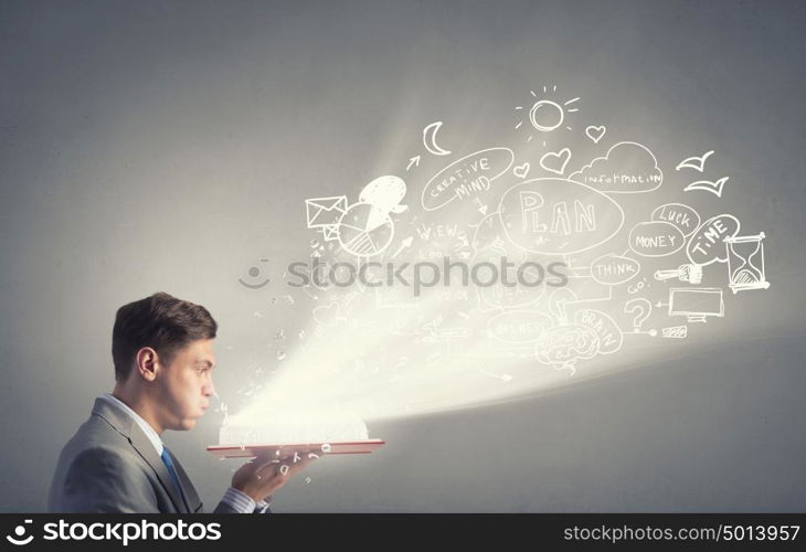 Business education. Young businessman with opened book in hands blowing on pages