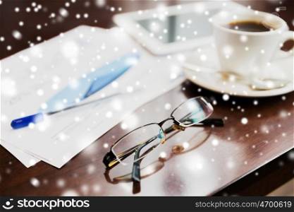 business, eyewear, optics and objects concept - eyeglasses, tablet pc, charts and coffee on office table over snow