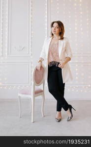 Business fashion woman in a classic suit with white jacket, black pants and high heels on white wall with light background. Business fashion woman in a classic suit with white jacket, black pants and high heels on white wall with light background.