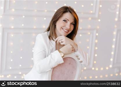 Business fashion woman in a classic suit with white jacket, black pants and high heels on white wall with light background.. Business fashion woman in a classic suit with white jacket, black pants and high heels on white wall with light background