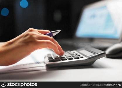 business, finance and accounting concept - close up of businesswoman with calculator counting and filling tax form at night office. businesswoman with calculator at night office