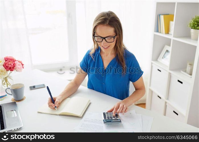 business, finance and accounting concept - middle-aged woman with calculator counting and writing to notebook at office. woman with calculator and notebook at office
