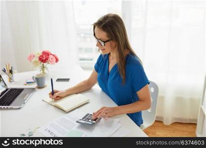 business, finance and accounting concept - middle-aged woman with calculator counting and writing to notebook at office. woman with calculator and notebook at office