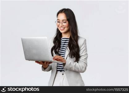 Business, finance and employment, female successful entrepreneurs concept. Professional stylish asian businesswoman fixing project on her way to office, using laptop standing whtie background.. Business, finance and employment, female successful entrepreneurs concept. Professional stylish asian businesswoman fixing project on her way to office, using laptop standing whtie background