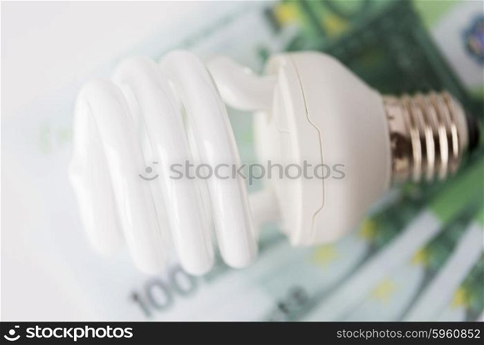 business, finance, energy saving and utilities concept - close up of euro paper money and light bulb on table