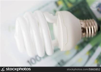 business, finance, energy saving and utilities concept - close up of euro paper money and light bulb on table