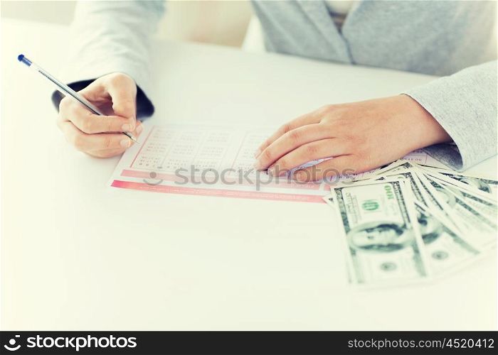 business, finance, gambling and people concept - close up of woman hands filling lottery ticket and us dollar money
