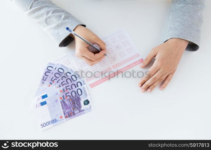 business, finance, gambling and people concept - close up of woman hands filling lottery ticket and money