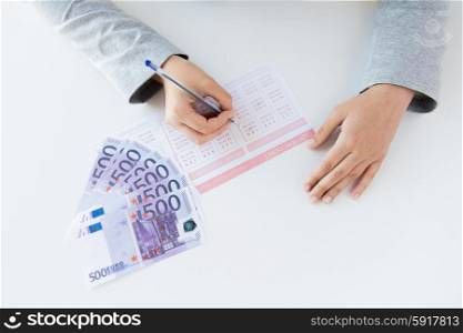 business, finance, gambling and people concept - close up of woman hands filling lottery ticket and money