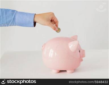 business, finance, investment, money saving and budget concept - close up of hand putting coin into piggy bank