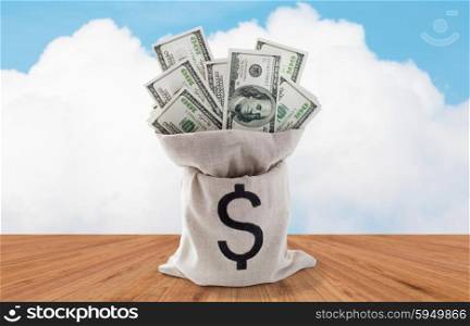business, finance, investment, saving and cash concept - close up of dollar paper money in bag over wooden floor and blue sky background