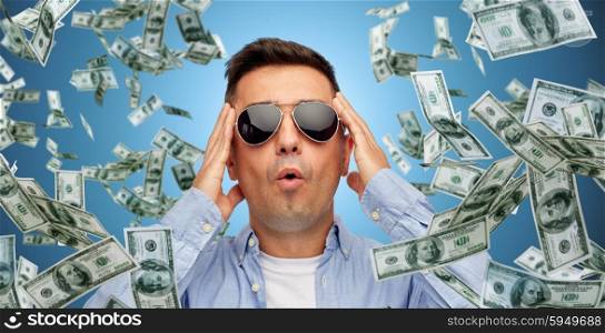 business, finance, luck, fortune and people concept - face of scared or surprised middle aged latin man in sunglasses over blue background with heap of falling dollar money