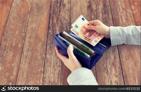 business, finance, saving, banking and people concept - close up of woman hands with wallet and euro money on wooden table