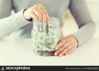 business, finance, saving, banking and people concept - close up of woman hands putting us dollar money into glass mason jar