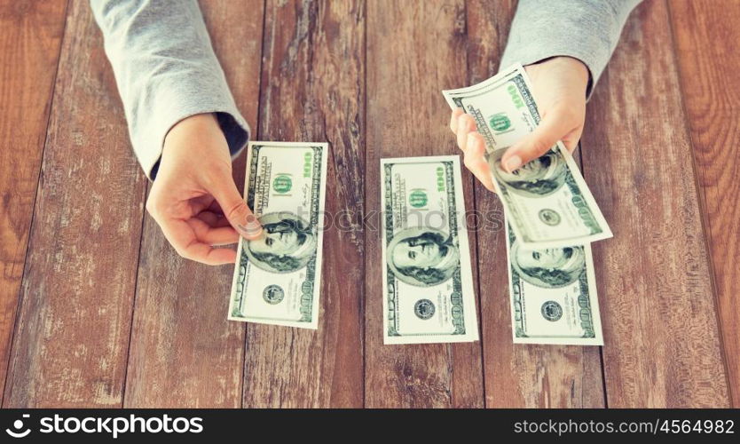 business, finance, saving, banking and people concept - close up of woman hands counting us dollar money on wooden table