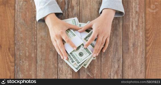 business, finance, saving, banking and people concept - close up of woman hands counting us dollar money on wooden table