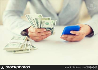 business, finance, saving, technology and people concept - close up of woman hands with smartphone and us dollar money