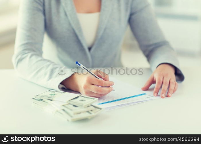 business, finance, tax and people concept - close up of woman hands with us dollar money filling tax paper form