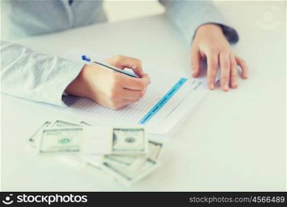 business, finance, tax and people concept - close up of woman hands with us dollar money filling tax paper form
