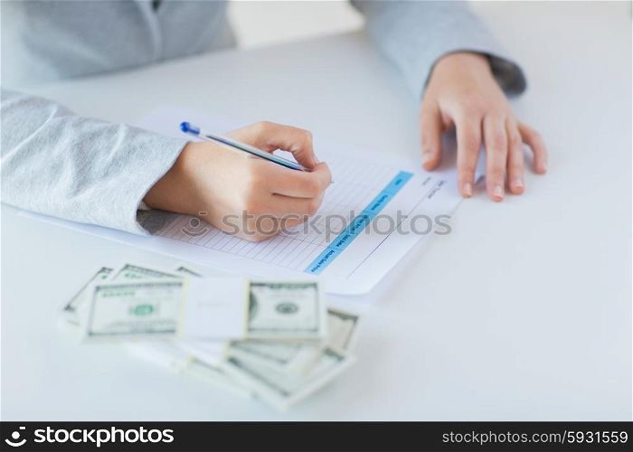 business, finance, tax and people concept - close up of woman hands with us dollar money filling tax paper form