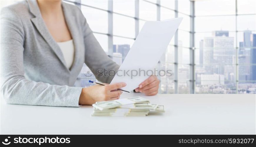 business, finance, tax and people concept - close up of woman hands with us dollar money and tax report paper form over city office room background