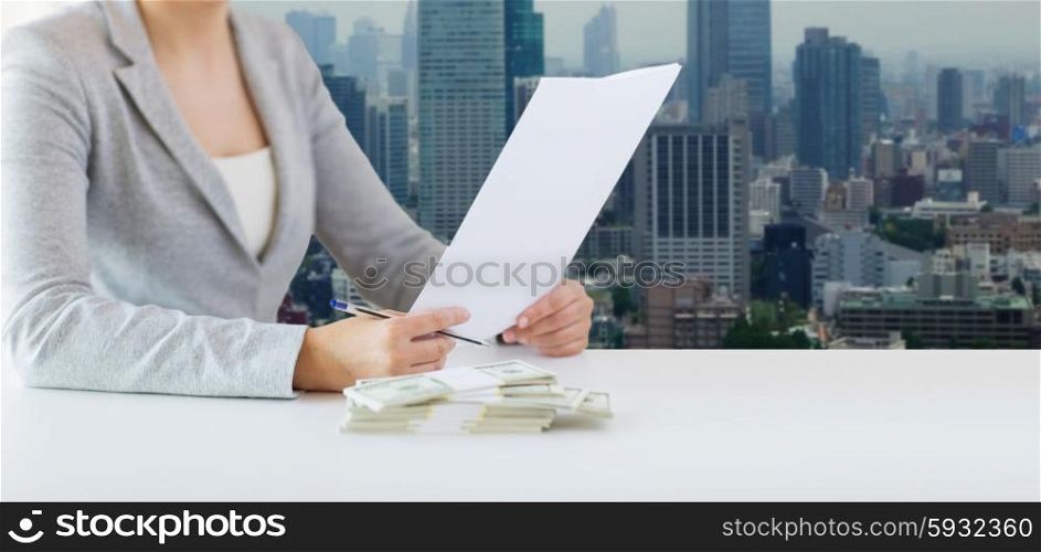 business, finance, tax and people concept - close up of woman hands with us dollar money and tax report paper form over city background