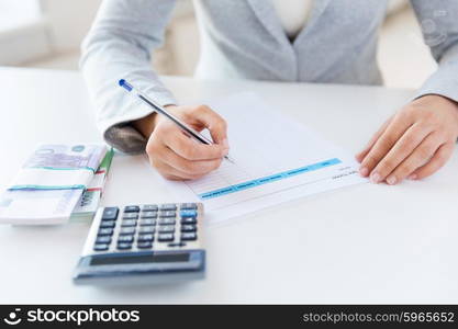 business, finance, tax and people concept - close up of woman hands counting euro money with calculator and tax report form