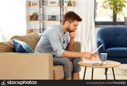 business, finances, accounting and people concept - man with calculator counting and filling papers at home. man with bills counting on calculator at home