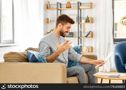 business, finances, accounting and people concept - man with calculator counting and filling papers at home. man with bills counting on calculator at home