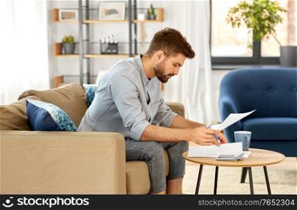 business, finances, accounting and people concept - man with calculator counting and filling papers at home. man with bills counting on calculator at home