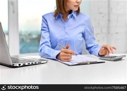 business, finances and accounting concept - close up of businesswoman with laptop computer and calculator filling papers at office. businesswoman with papers, laptop and calculator
