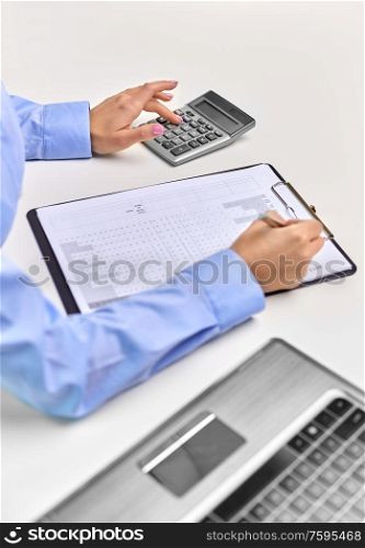 business, finances and accounting concept - close up of businesswoman with laptop computer and calculator filling papers at office. businesswoman with papers, laptop and calculator