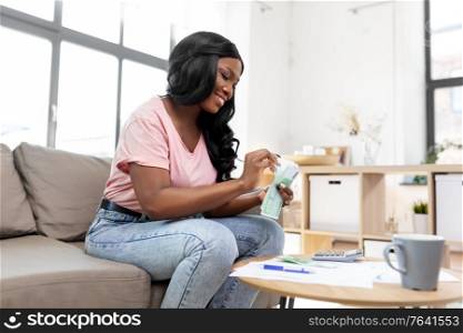 business, finances, income and people concept - happy smiling african american woman counting money at home. african american woman counting money at home