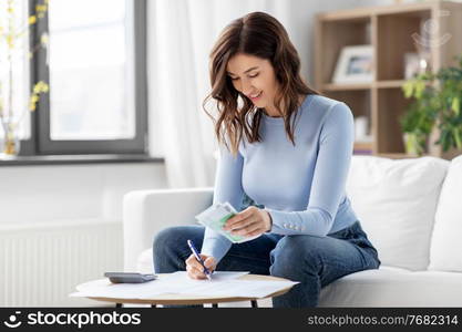 business, finances, income and people concept - happy smiling woman with calculator and bills counting money at home. happy woman counting money at home