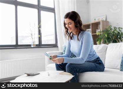 business, finances, income and people concept - happy smiling woman with calculator and bills counting money at home. happy woman counting money at home