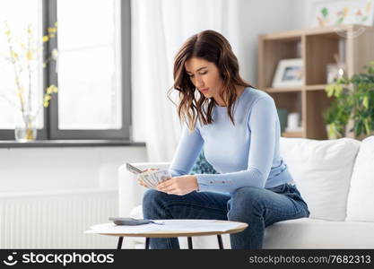 business, finances, income and people concept - woman with calculator and bills counting money at home. woman counting money at home