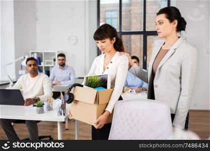 business, firing and job loss concept - colleague seeing off sad fired asian female office worker holding box of his personal stuff. colleague soothing sad fired female office worker
