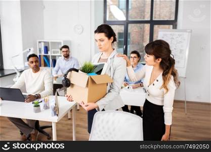 business, firing and job loss concept - colleague seeing off sad fired female office worker holding box of his personal stuff. colleague soothing sad fired female office worker