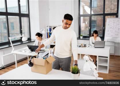business, firing and job loss concept - sad fired indian male office worker packing his personal stuff. sad fired office worker packing personal stuff